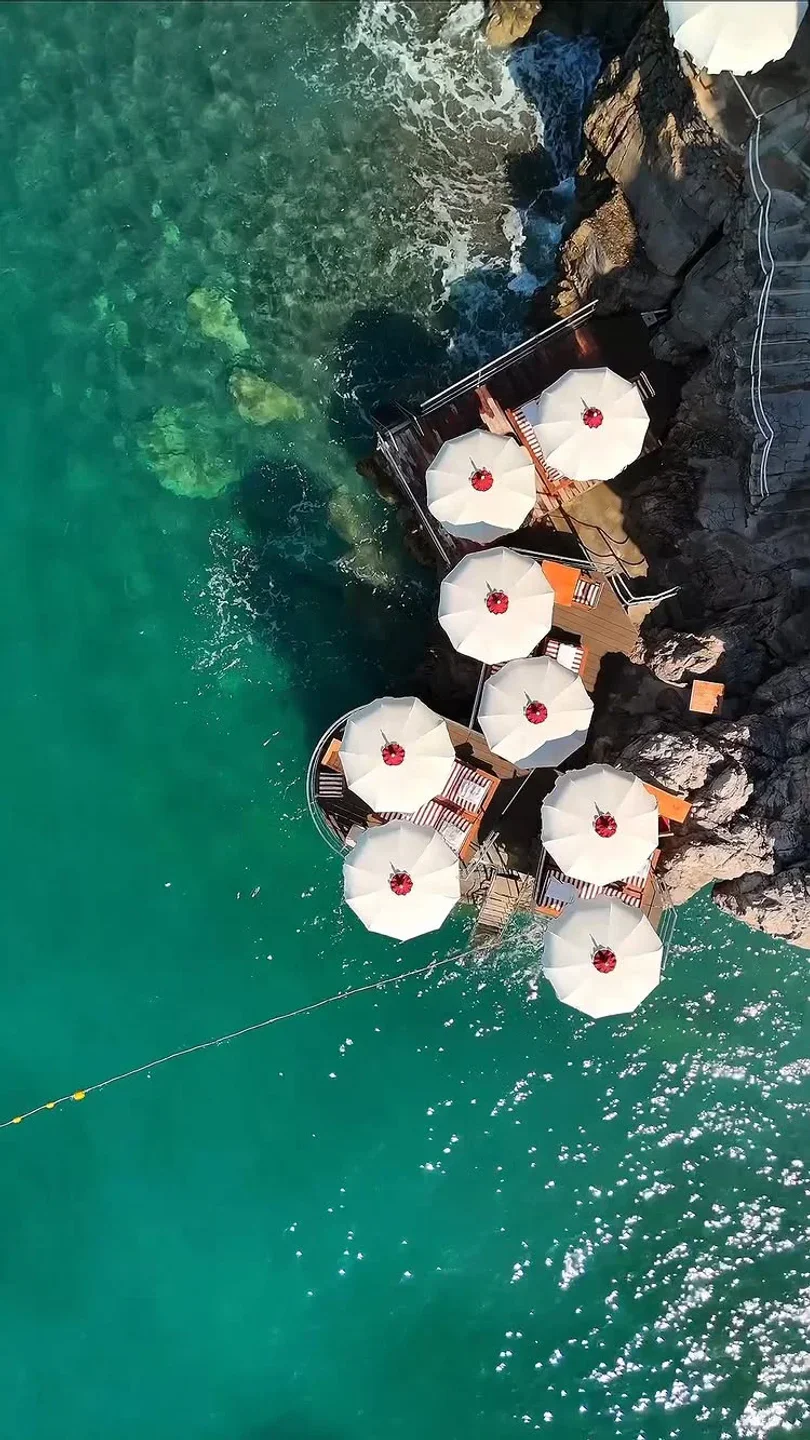 La Scogliera Positano restaurant exterior with umbrellas on wooden deck overlooking turquoise Amalfi Coast waters.